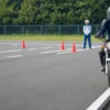 自動車教習所の一本橋を低速で走行する初心者ライダーと見守る指導員