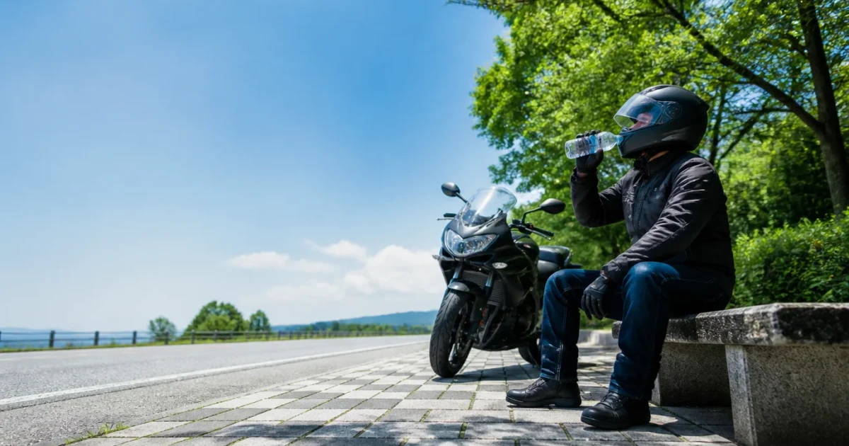 真夏の休憩スペースでバイクを停めて水分補給するライダー
